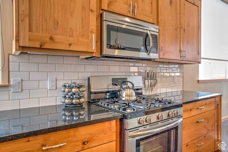 Kitchen featuring appliances with stainless steel finishes, decorative backsplash, brown cabinetry, and dark stone counters