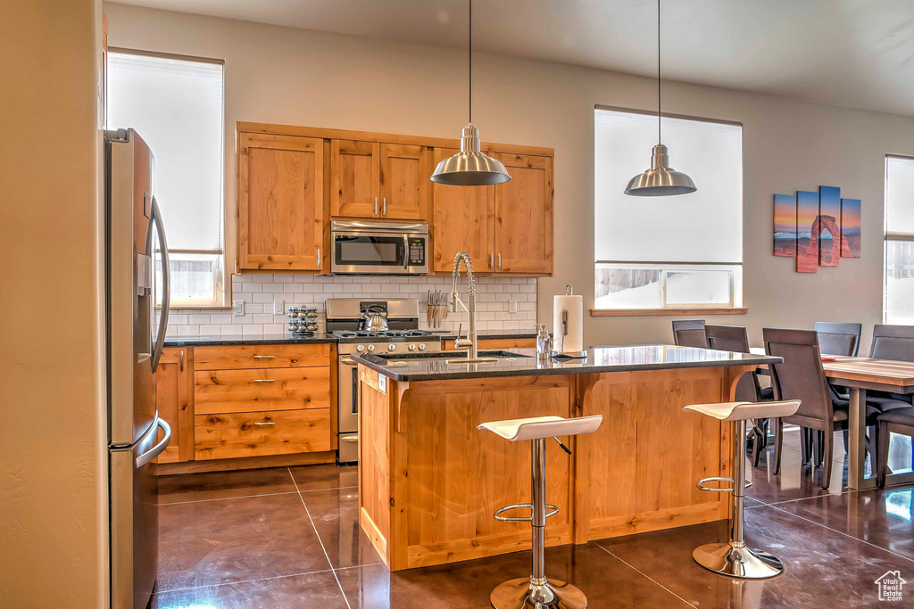 Kitchen with appliances with stainless steel finishes, decorative backsplash, dark tile patterned floors, and a sink