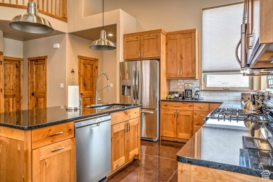 Kitchen featuring stainless steel appliances, a sink, tasteful backsplash, a kitchen island with sink, and dark tile patterned floors