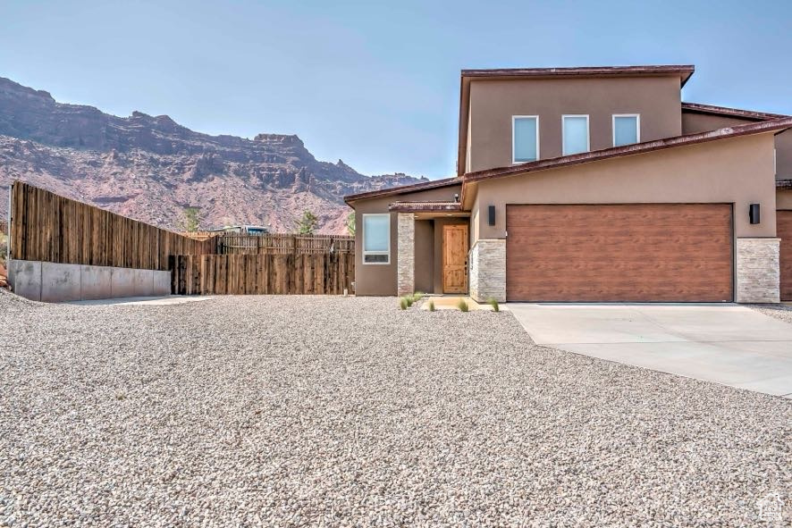 View of front of home with stucco siding, concrete driveway, a mountain view, stone siding, and an attached garage