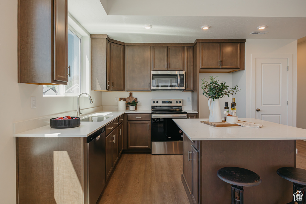 Kitchen with appliances with stainless steel finishes, wood finished floors, light countertops, a kitchen island, and recessed lighting