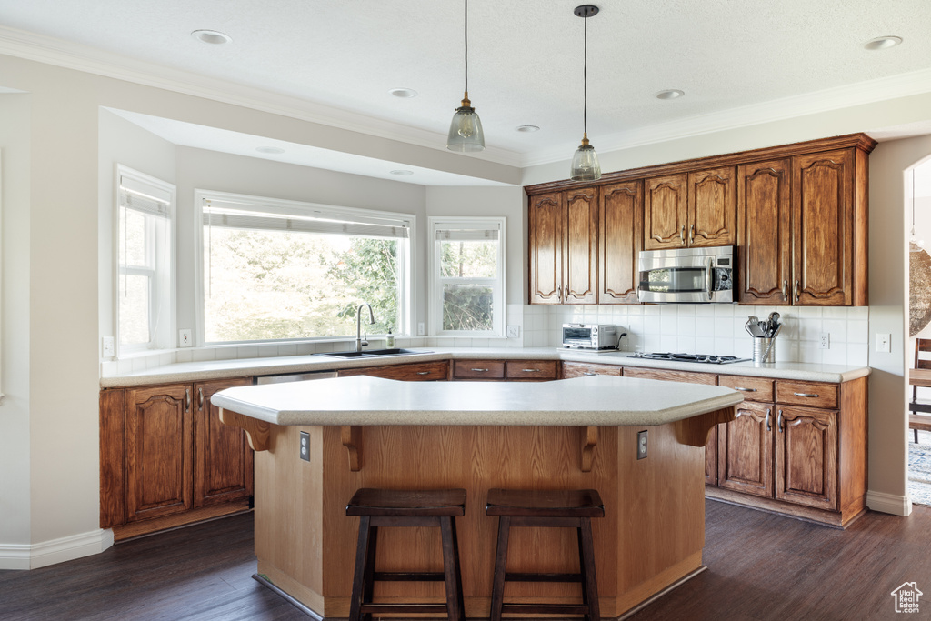 Kitchen featuring stainless steel microwave, a kitchen island, dark wood finished floors, light countertops, and backsplash