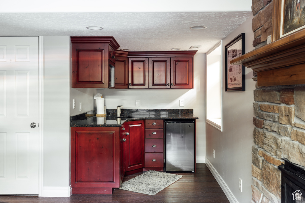 Indoor wet bar featuring dark wood-type flooring, a textured ceiling, and dishwashing machine