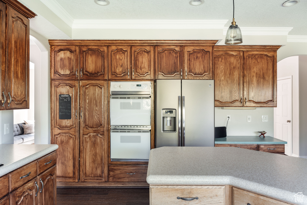 Kitchen with stainless steel fridge, double oven, arched walkways, crown molding, and dark wood-style flooring
