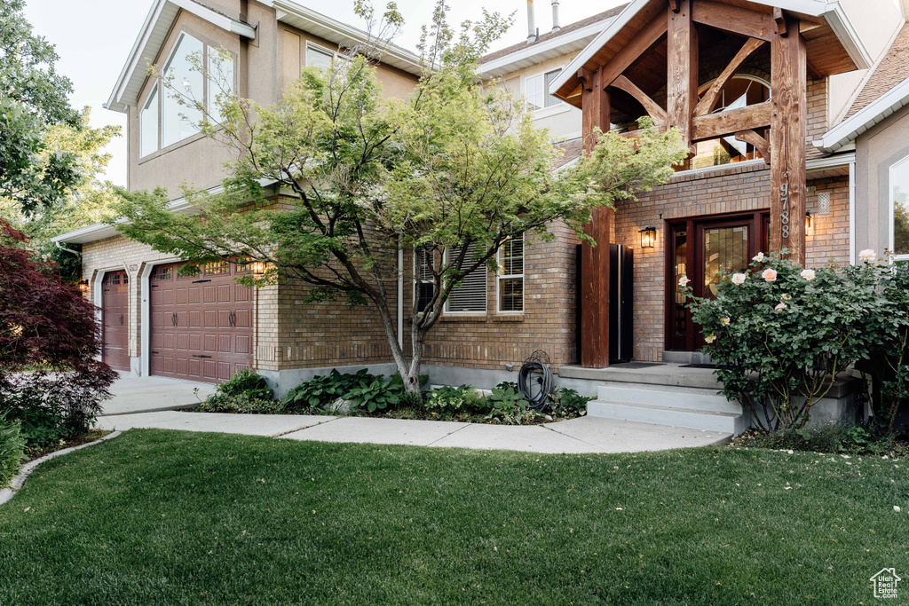 View of front of home with brick siding, a front yard, and a garage