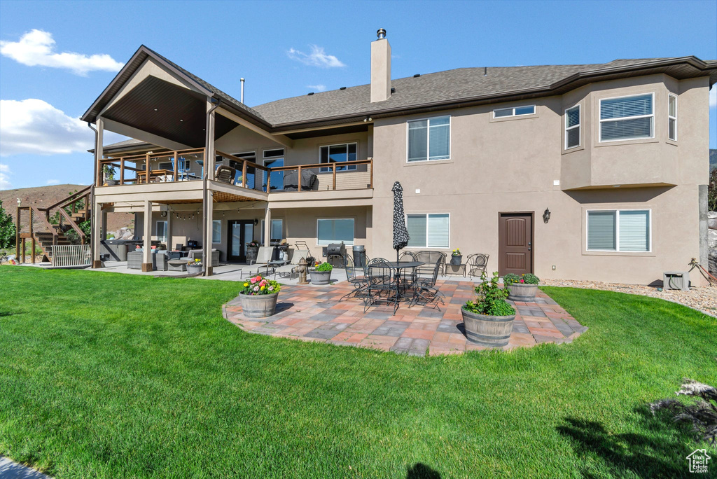 Rear view of house with a chimney, stucco siding, a yard, a patio area, and a balcony
