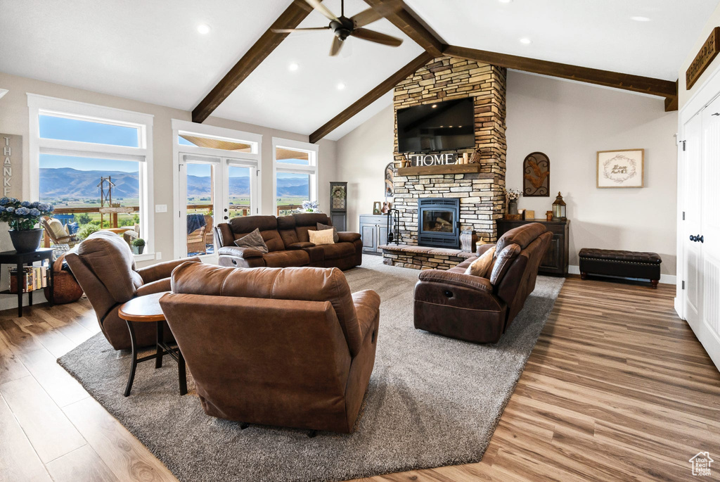 Living room with ceiling fan, wood finished floors, beam ceiling, a stone fireplace, and plenty of natural light