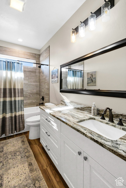 Bathroom with double vanity, shower / bathtub combination with curtain, and wood finished floors