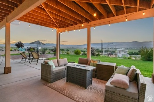 Patio terrace at dusk featuring an outdoor living space with a fire pit, a patio, a yard, and a mountain view