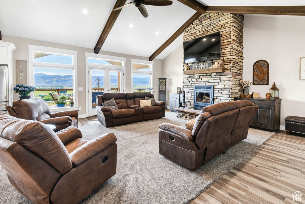 Living room with light wood-style floors, a ceiling fan, a fireplace, beamed ceiling, and high vaulted ceiling