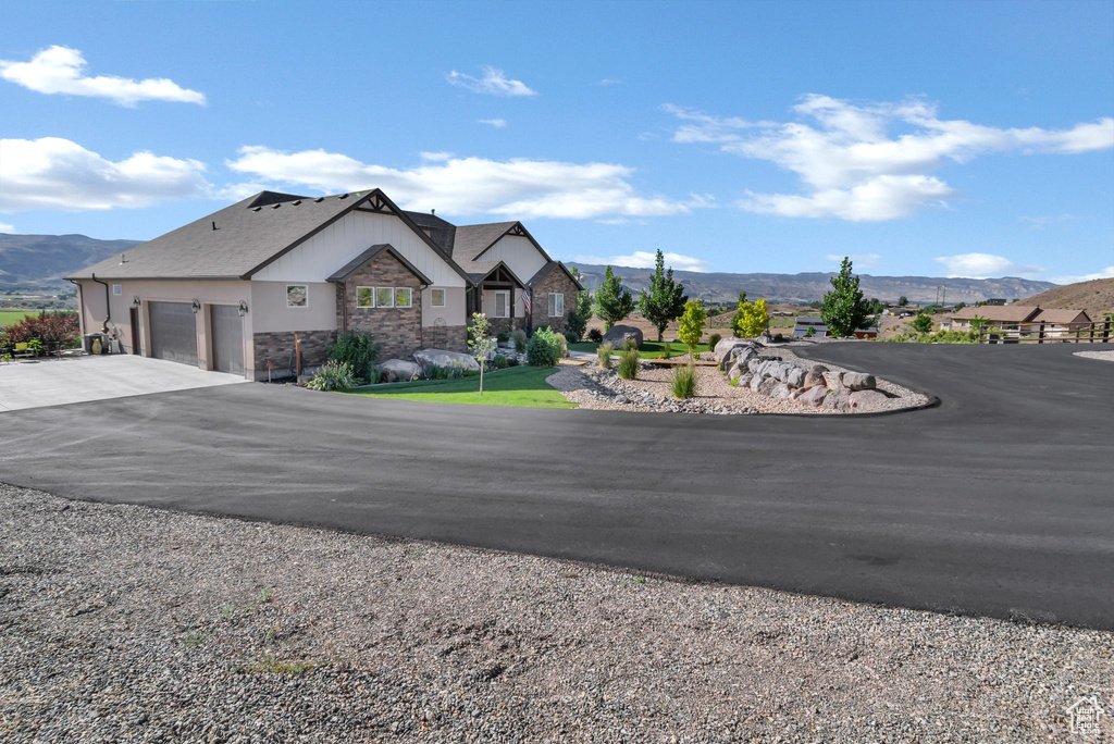 View of front of home featuring stone siding, a garage, a mountain view, and asphalt driveway