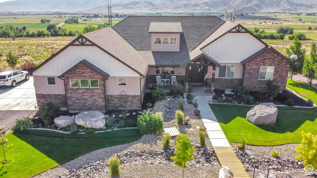 Craftsman-style home featuring stone siding, a shingled roof, a mountain view, and a front lawn