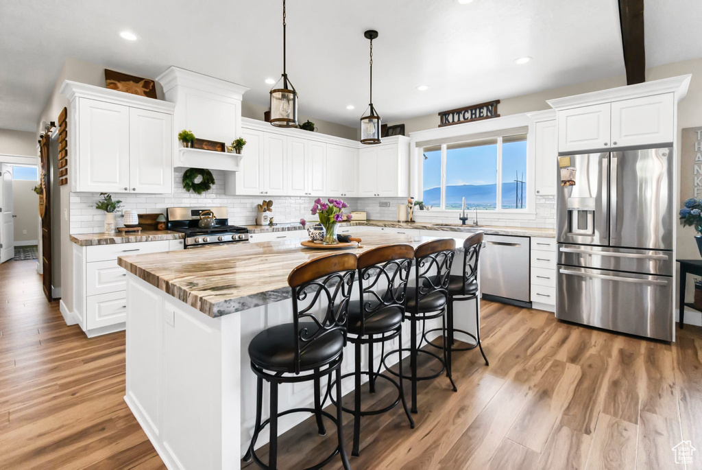 Kitchen with appliances with stainless steel finishes, a kitchen island, a kitchen bar, white cabinetry, and tasteful backsplash