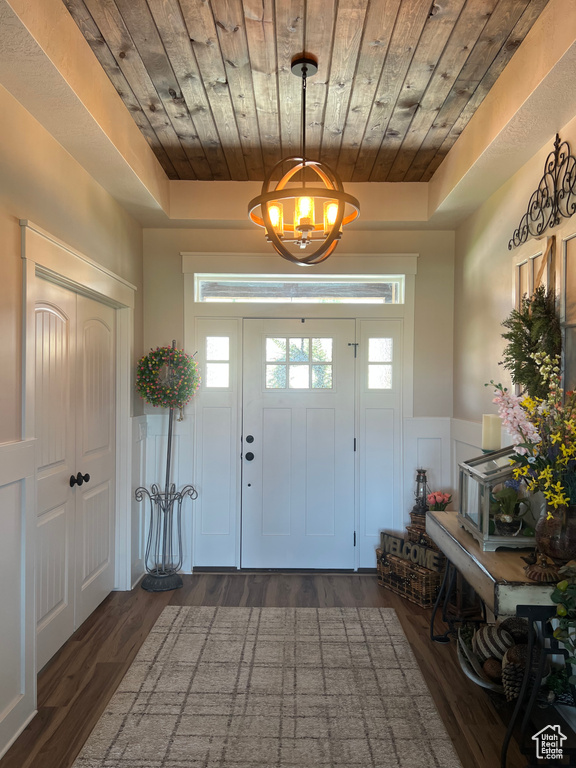 Foyer entrance featuring wooden ceiling, a wainscoted wall, dark wood finished floors, a chandelier, and a raised ceiling