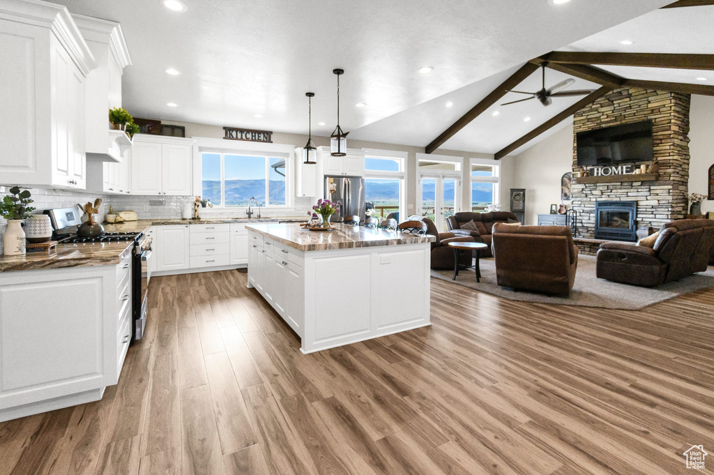 Kitchen featuring appliances with stainless steel finishes, ceiling fan, a kitchen island, wood finished floors, and open floor plan
