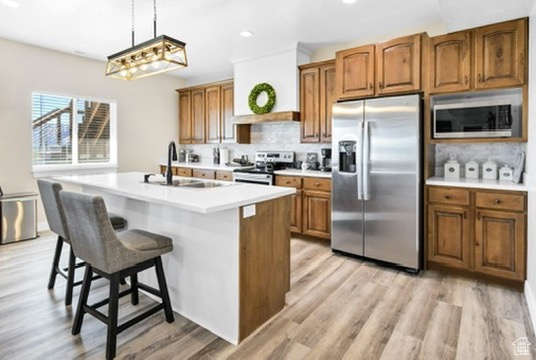 Kitchen featuring stainless steel appliances, decorative backsplash, light countertops, brown cabinetry, and recessed lighting