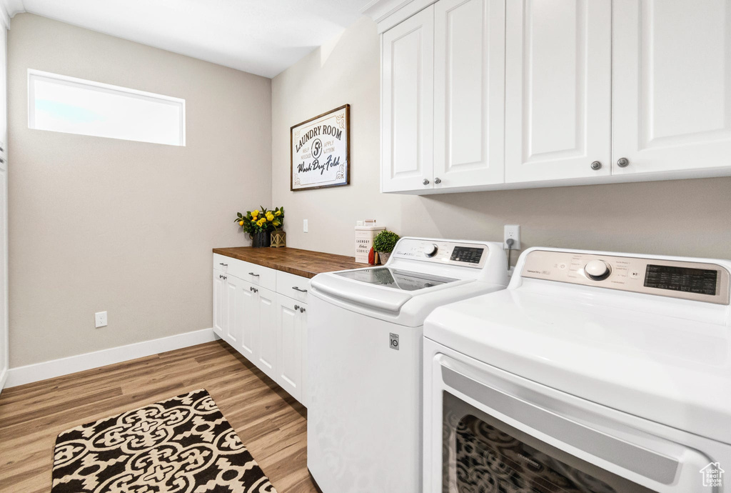 Laundry area featuring washer and dryer, cabinet space, and light wood-style flooring