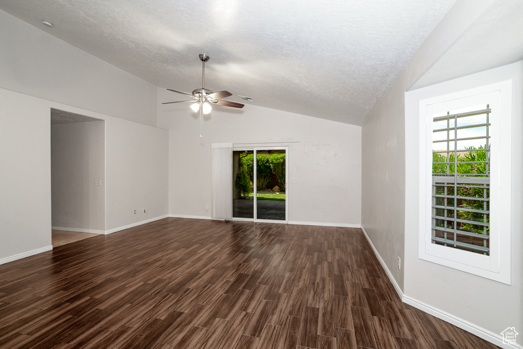 Empty room with ceiling fan, vaulted ceiling, dark wood finished floors, and a textured ceiling