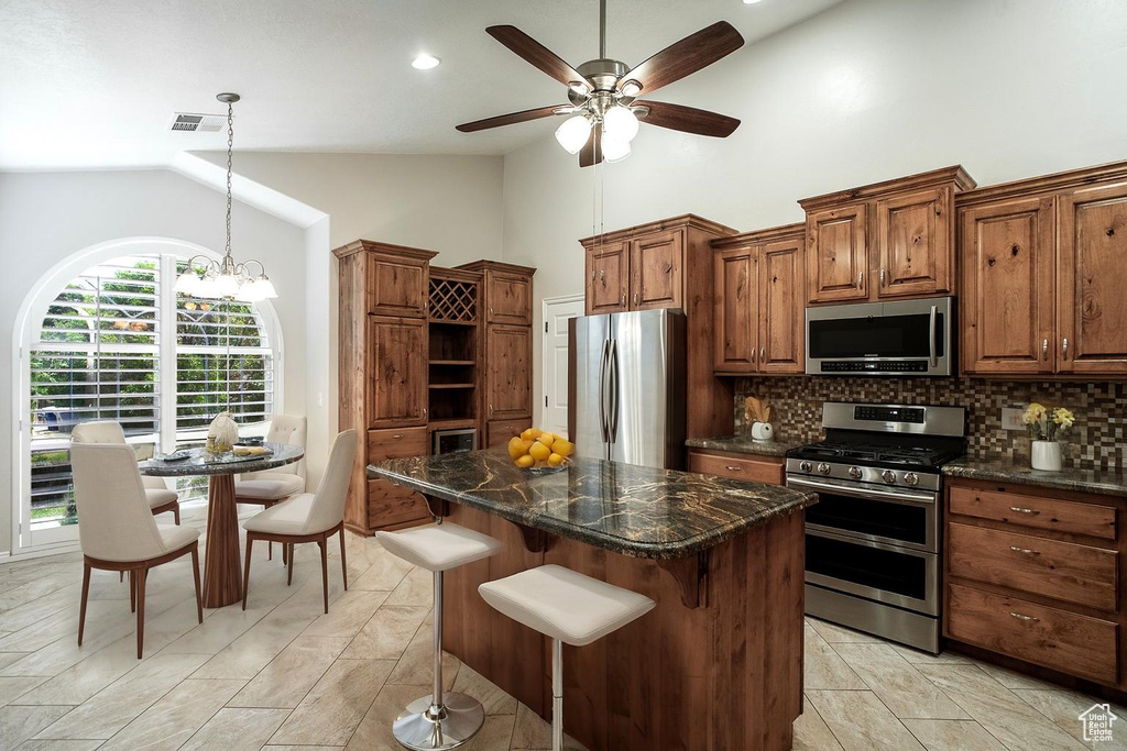 Kitchen featuring stainless steel appliances, tasteful backsplash, high vaulted ceiling, a center island, and ceiling fan