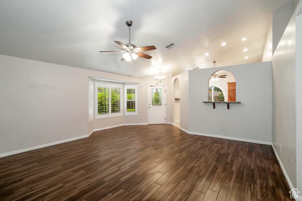 Empty room featuring a ceiling fan, dark wood-type flooring, arched walkways, a chandelier, and recessed lighting