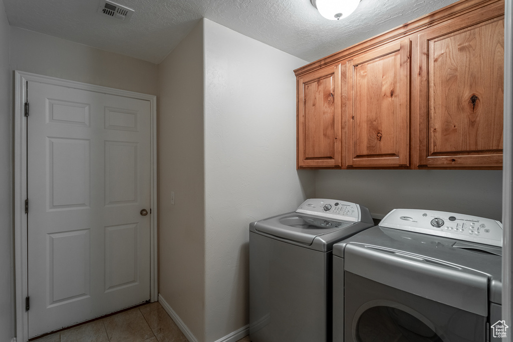 Laundry room featuring washing machine and dryer, cabinet space, light tile patterned flooring, and a textured ceiling