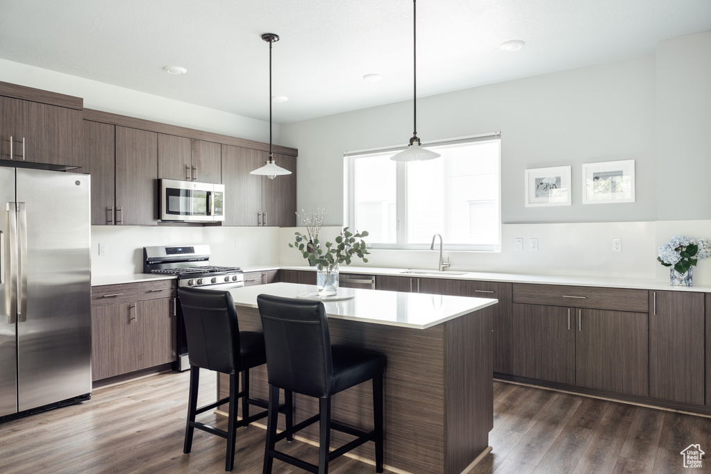 Kitchen with appliances with stainless steel finishes, a sink, a breakfast bar, dark wood-style floors, and recessed lighting