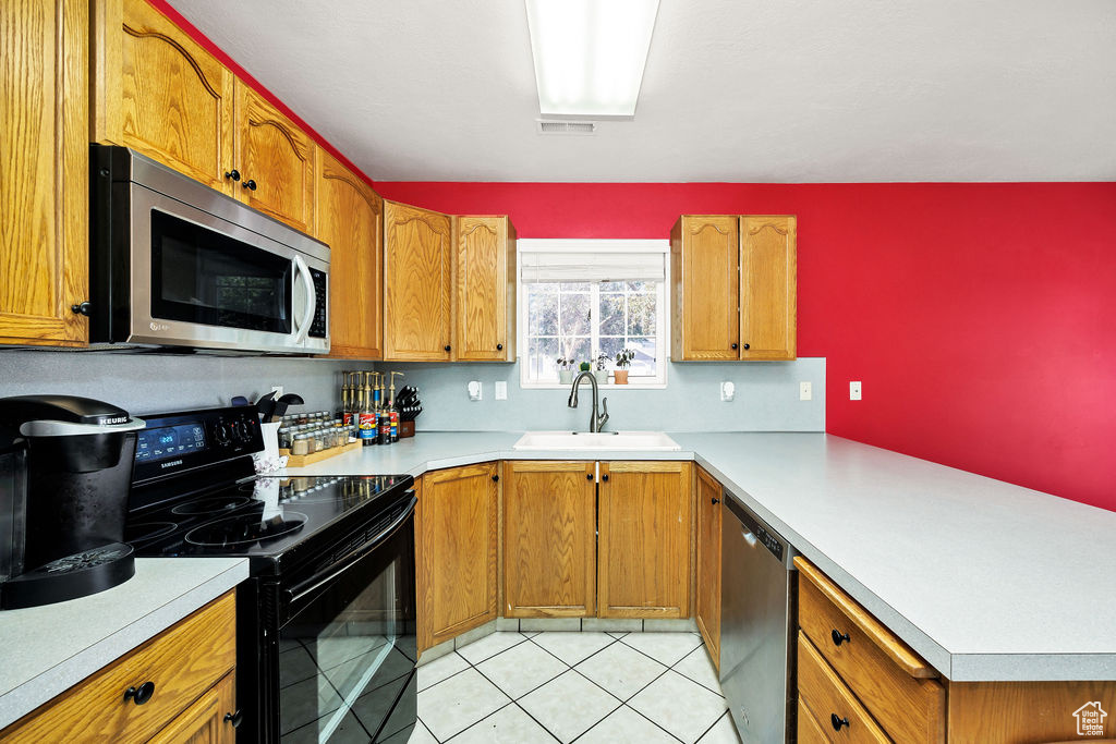 Kitchen with appliances with stainless steel finishes, a peninsula, light countertops, and brown cabinets