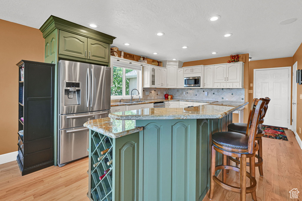 Kitchen with stainless steel appliances, green cabinets, light wood-style floors, tasteful backsplash, and a center island