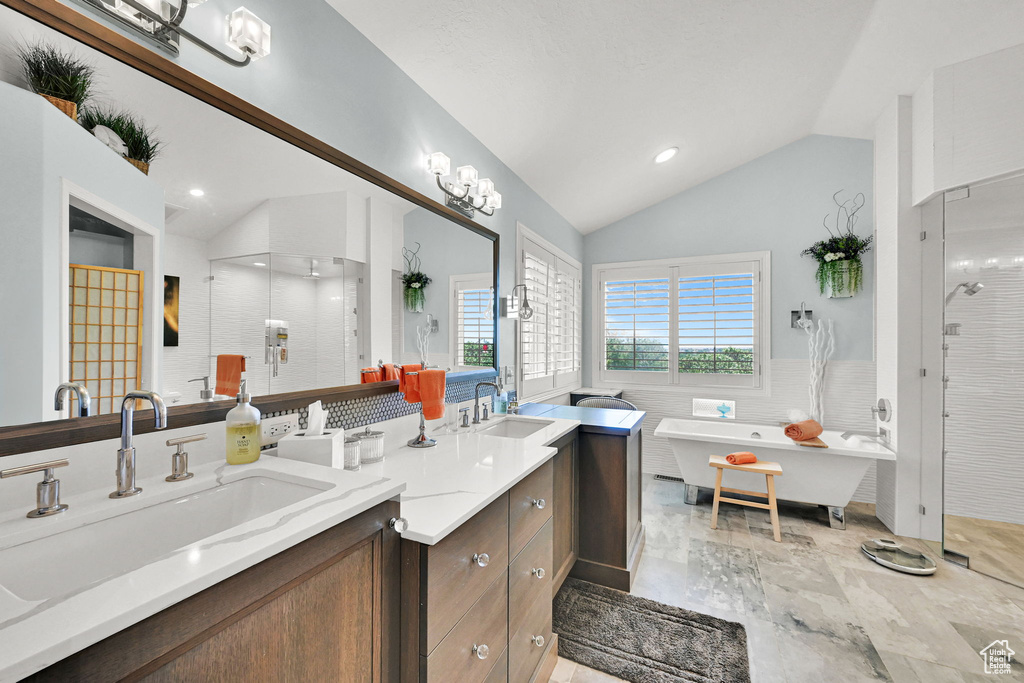 Full bathroom with lofted ceiling, double vanity, a stall shower, a wainscoted wall, and a soaking tub