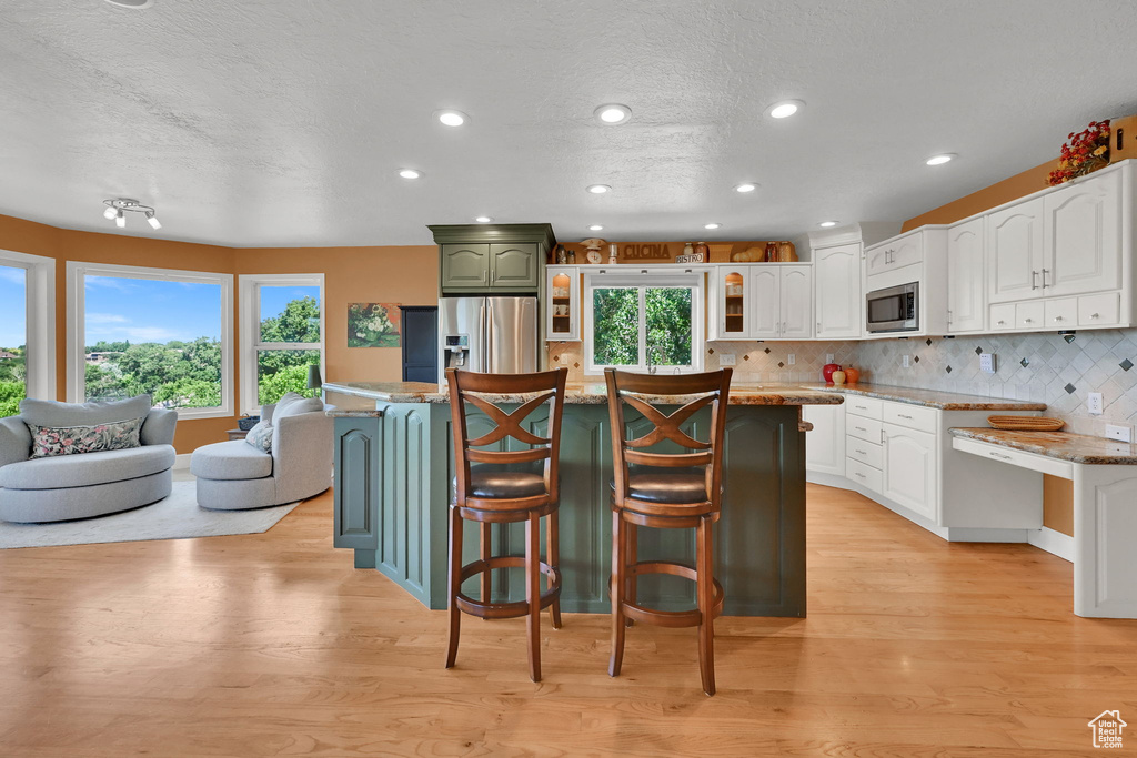 Kitchen featuring stainless steel appliances, a kitchen breakfast bar, light wood-style flooring, a textured ceiling, and white cabinets
