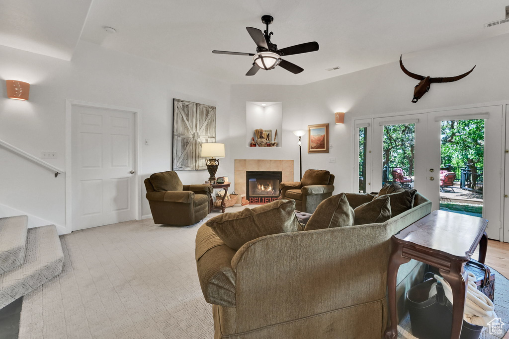 Living area with a tile fireplace, stairs, a ceiling fan, and light carpet