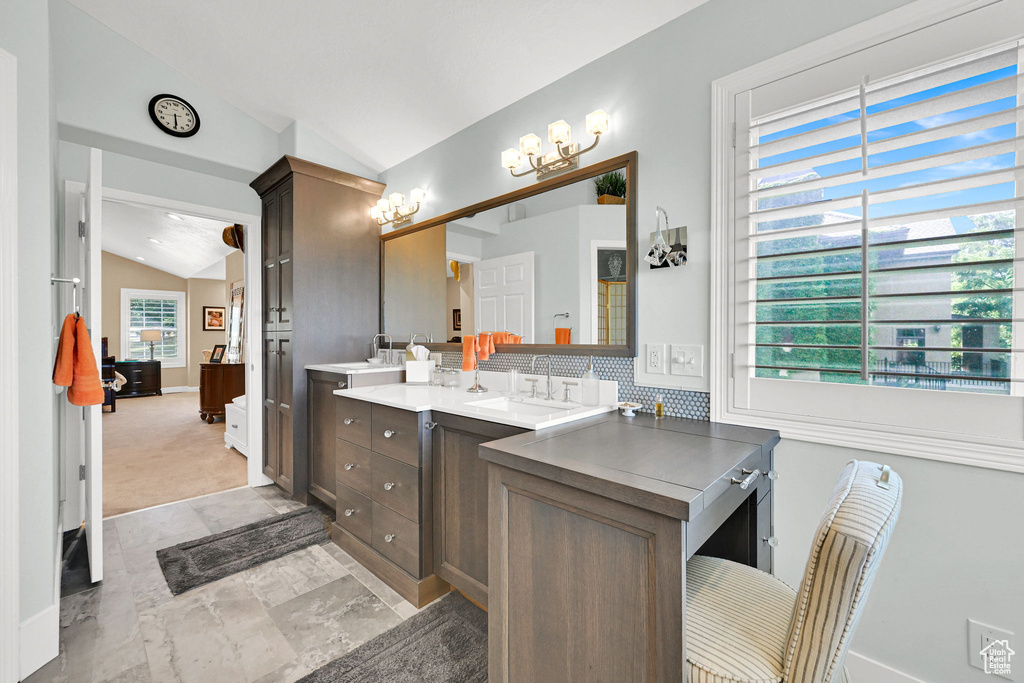 Full bath with lofted ceiling, double vanity, a chandelier, and backsplash