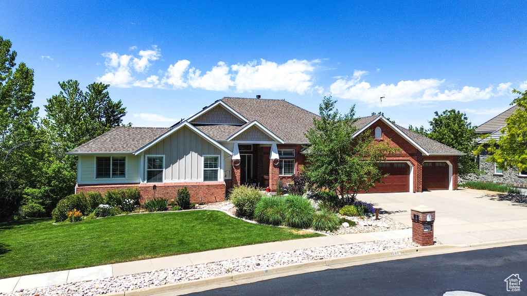 Craftsman-style house featuring board and batten siding, brick siding, driveway, a garage, and a front lawn