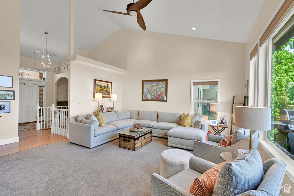 Carpeted living room featuring high vaulted ceiling, arched walkways, a ceiling fan, and wood finished floors