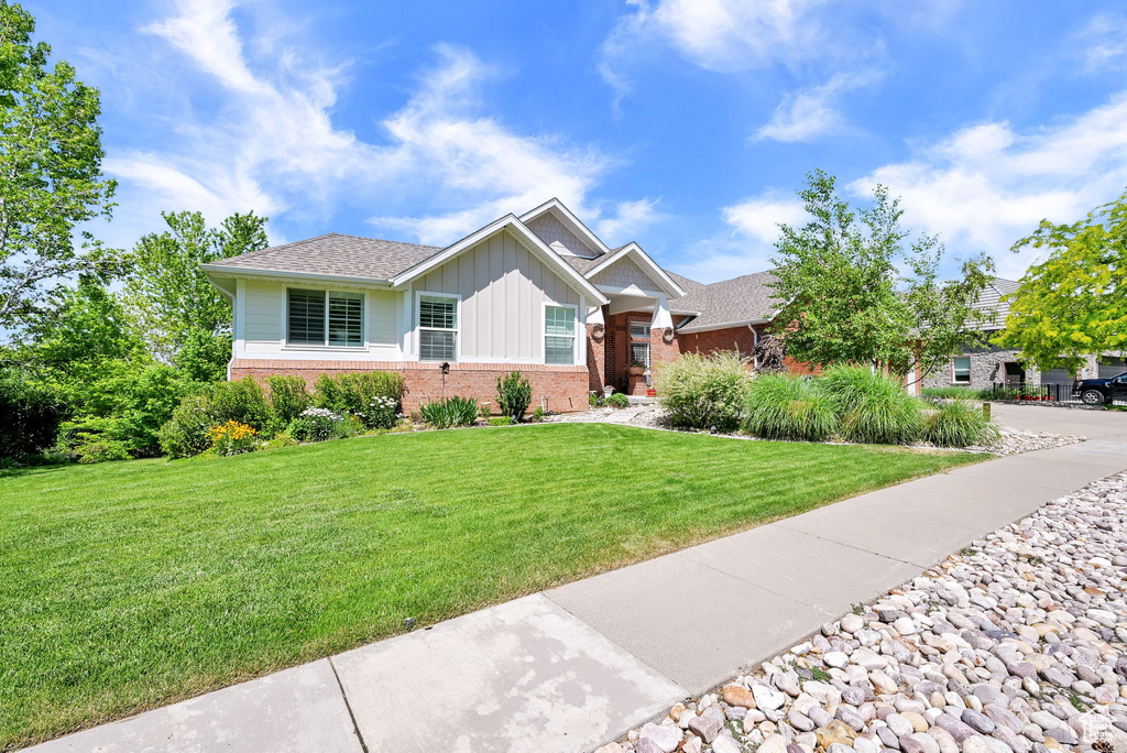 View of front of property with board and batten siding, brick siding, a front yard, and a shingled roof