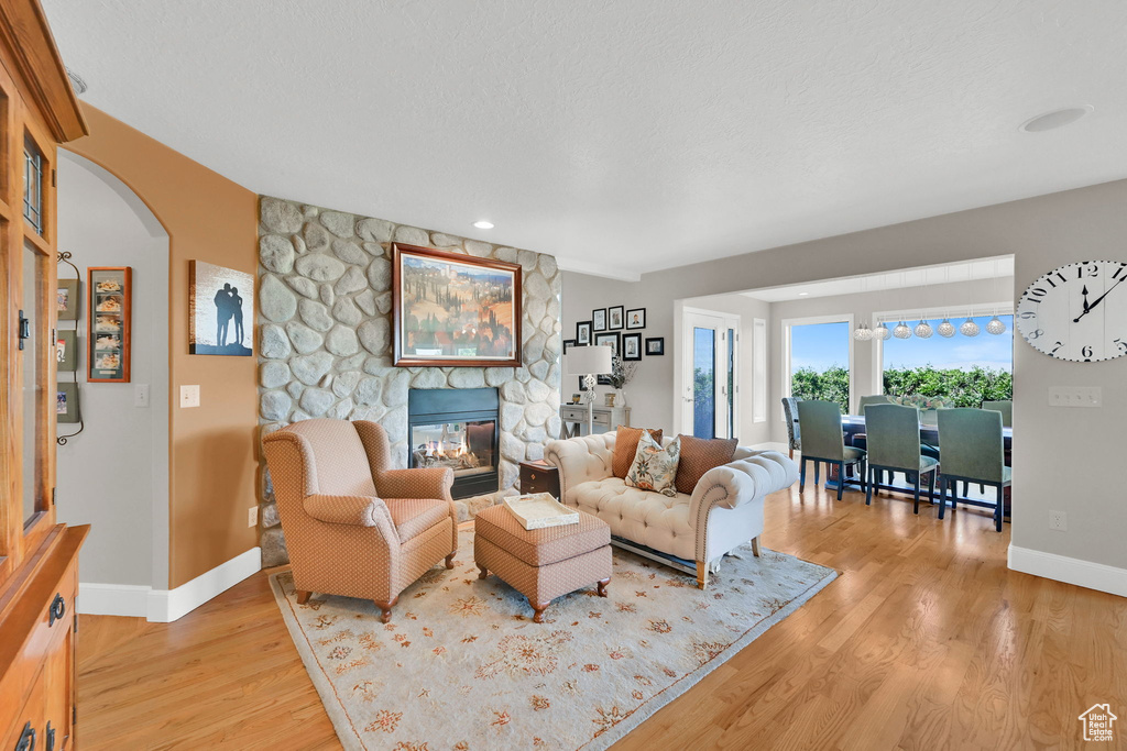 Living area featuring light wood-style floors, a stone fireplace, arched walkways, and recessed lighting