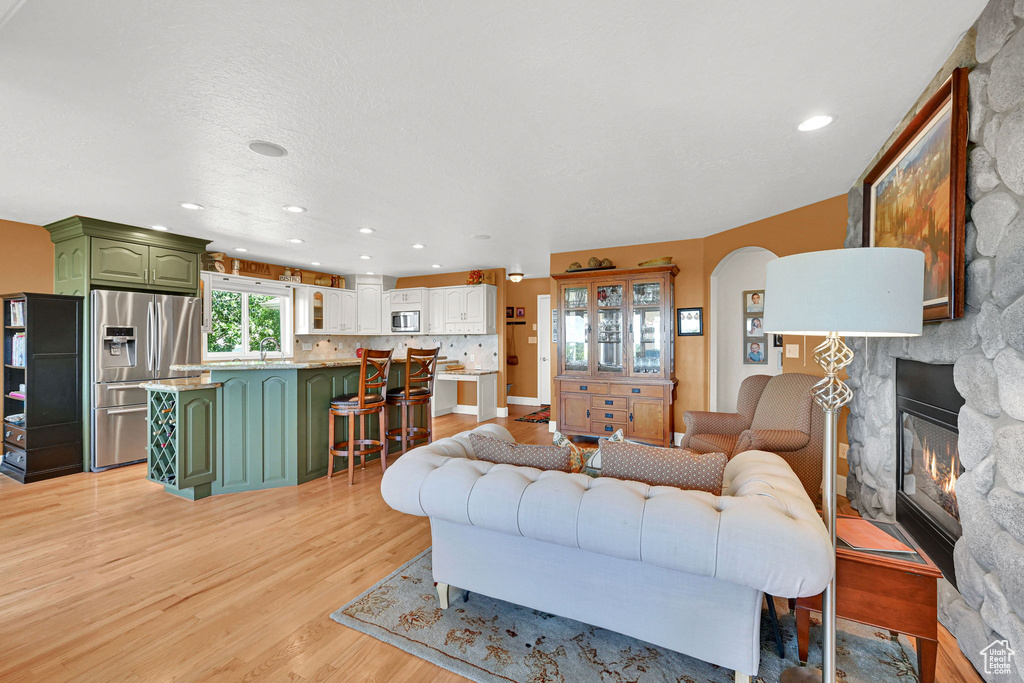 Living room with light wood-style flooring, a stone fireplace, recessed lighting, and arched walkways