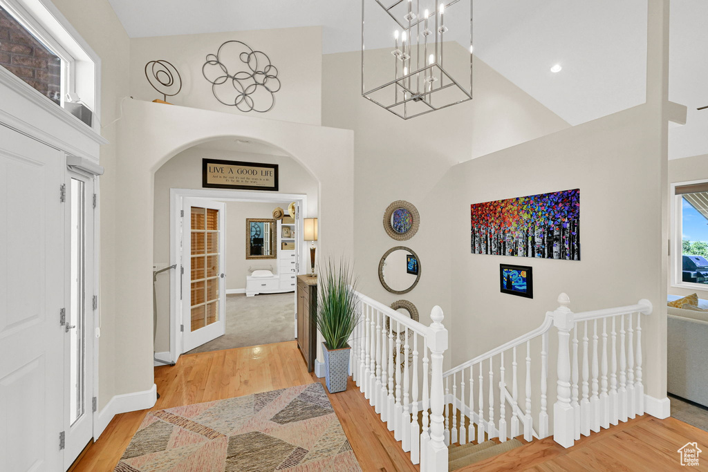 Foyer entrance with a towering ceiling, a chandelier, light wood-style flooring, and arched walkways