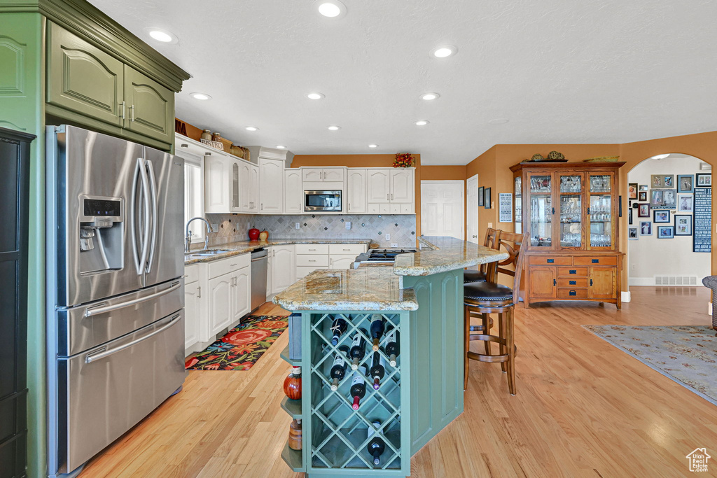 Kitchen featuring appliances with stainless steel finishes, arched walkways, light wood-type flooring, a breakfast bar, and green cabinetry