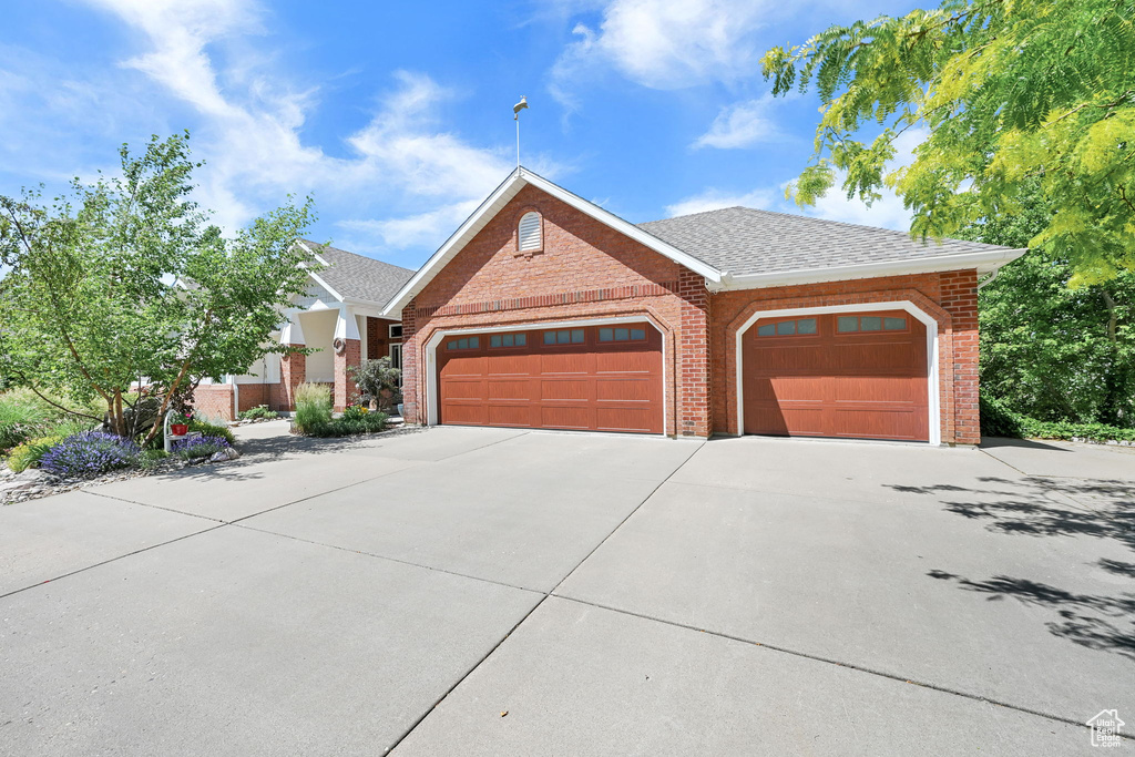 View of front facade with brick siding, a garage, driveway, and roof with shingles