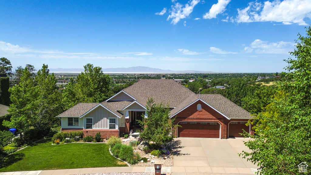 View of front of house with brick siding, an attached garage, board and batten siding, concrete driveway, and a front lawn