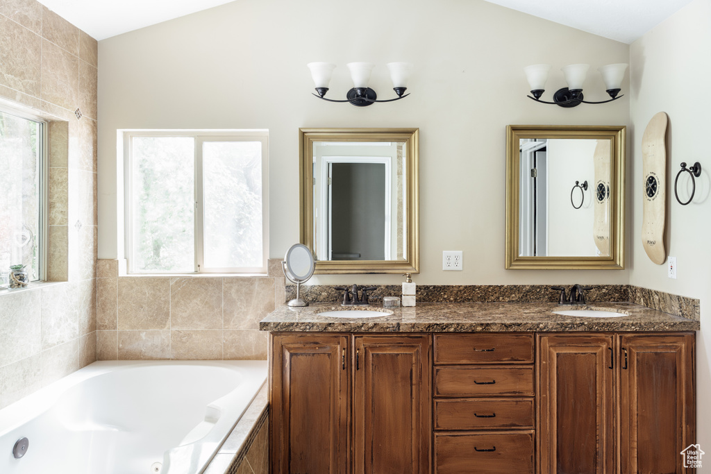 Full bath with plenty of natural light, double vanity, a bath, and lofted ceiling