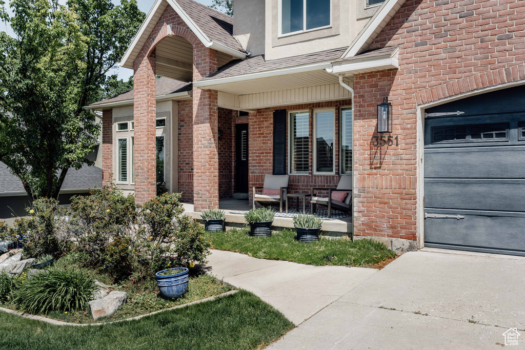 Doorway to property with covered porch, roof with shingles, and brick siding