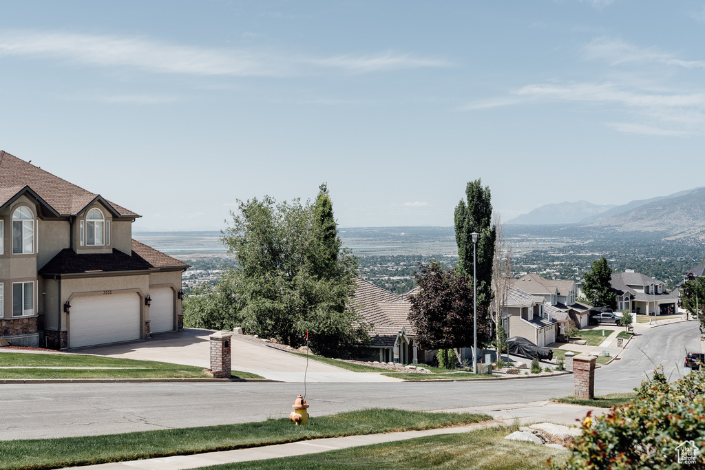 View of asphalt road featuring street lights, sidewalks, curbs, a mountain view, and a residential view