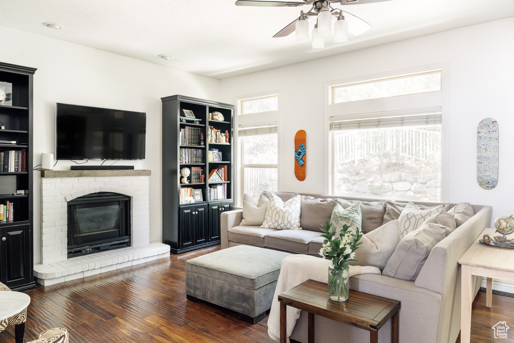 Living room with a ceiling fan, dark wood-style floors, and a brick fireplace
