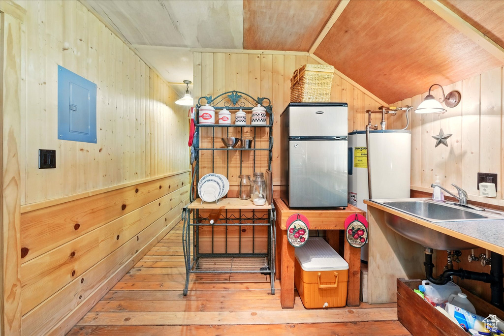 Kitchen featuring wooden walls, vaulted ceiling, freestanding refrigerator, electric panel, and hardwood / wood-style flooring