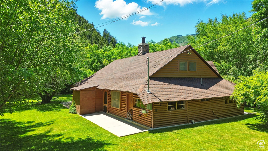 Rear view of house with a patio, a yard, a chimney, and a shingled roof