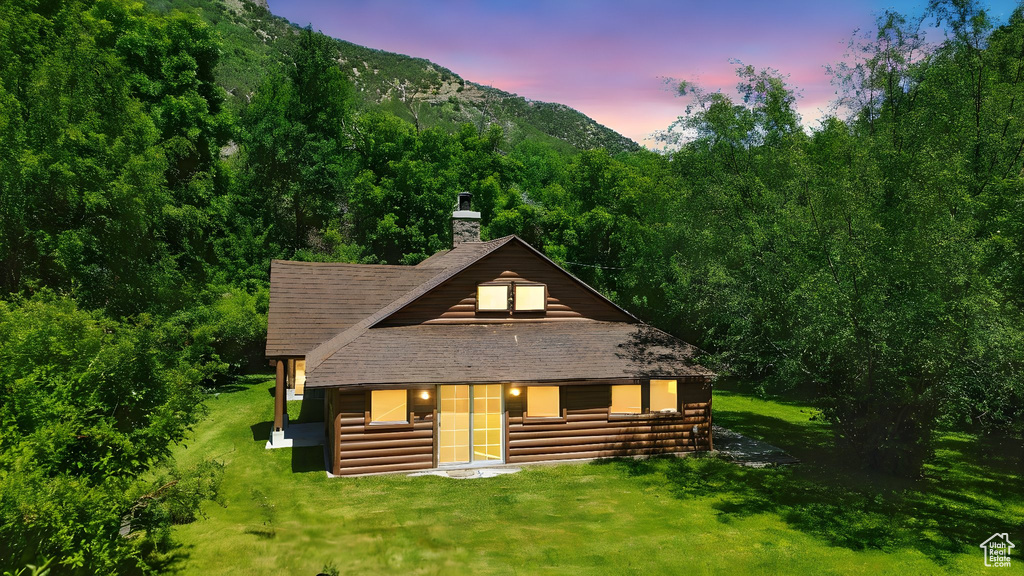 View of front of house featuring a chimney, a shingled roof, a mountain view, log veneer siding, and a front yard