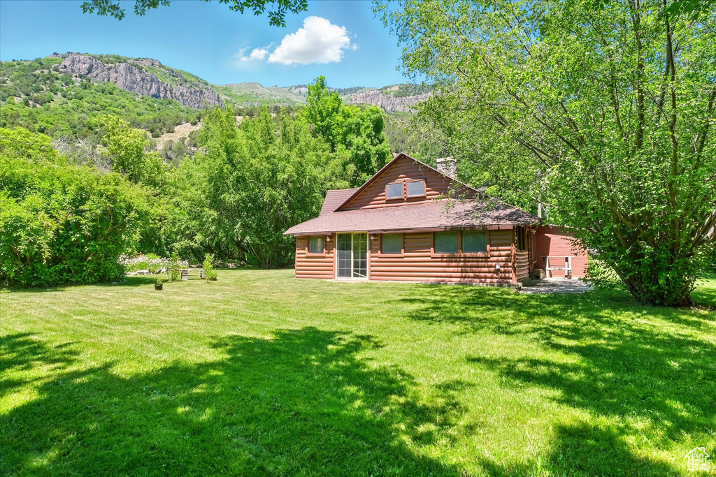 View of front of property featuring a front lawn, a view of trees, a chimney, and a mountain view