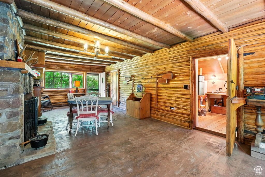 Dining room featuring log walls, hardwood / wood-style floors, a wooden ceiling with exposed beams, and a stone fireplace